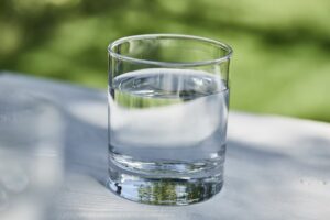 A clear glass filled with water sits on a white surface with a blurred green background.
