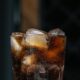 Glass of dark soda with ice cubes and fizzing bubbles on a dark background